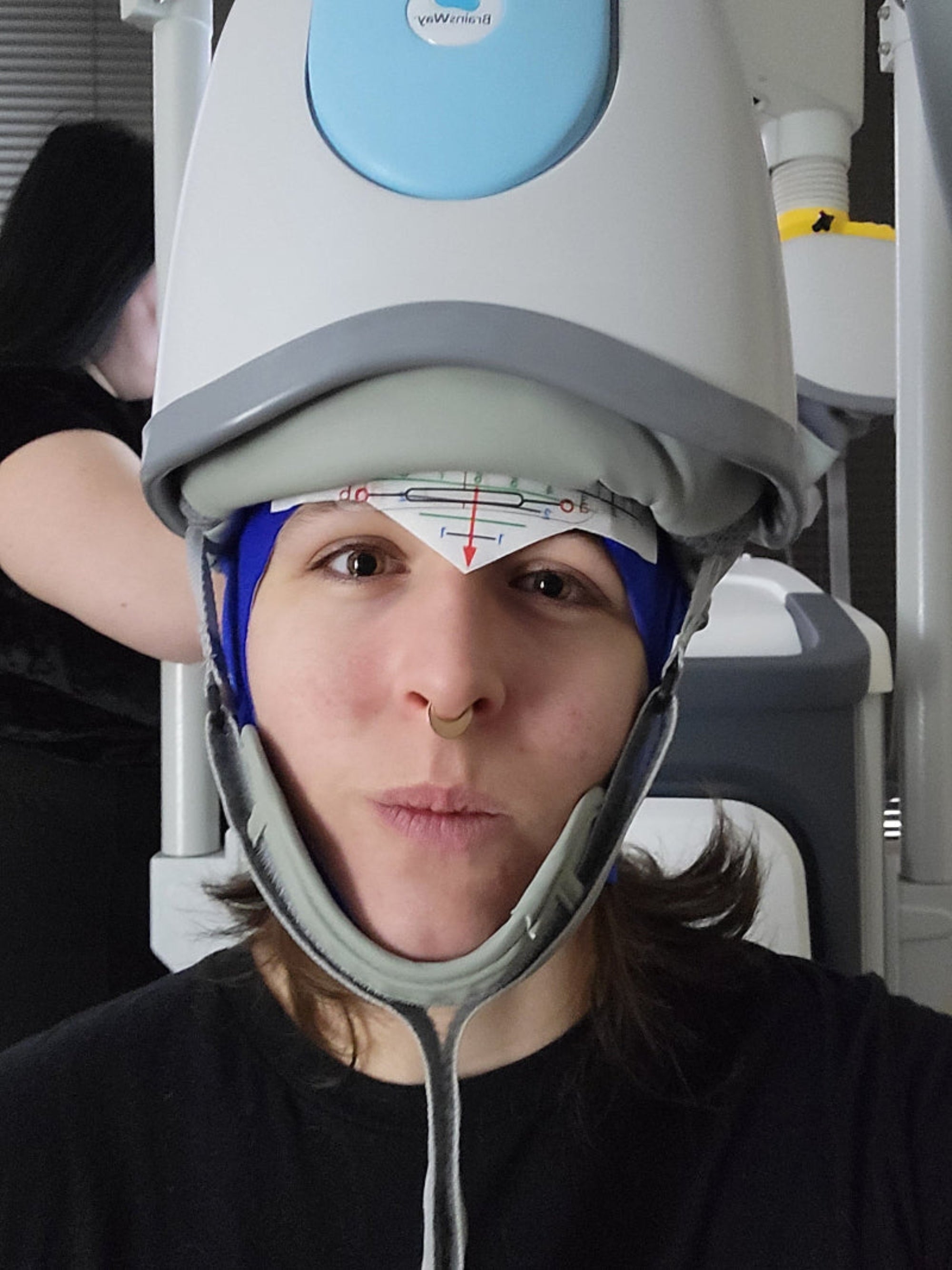 Person wearing a TMS helmet with medical equipment in the background